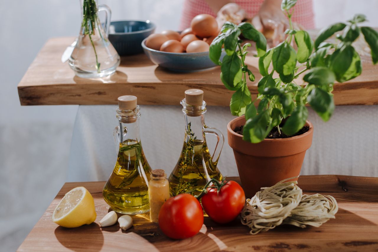 Fresh Italian cooking ingredients including olive oil, tomatoes, and basil on wooden tables.