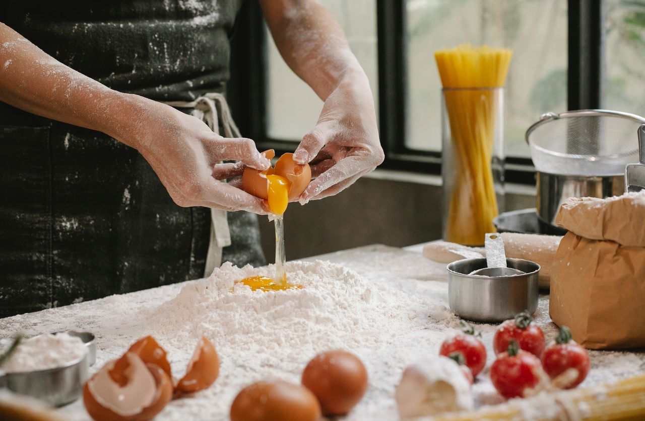 heros-img Crop anonymous person adding egg in flour while cooking pastry for recipe with cherry tomatoes and spaghetti