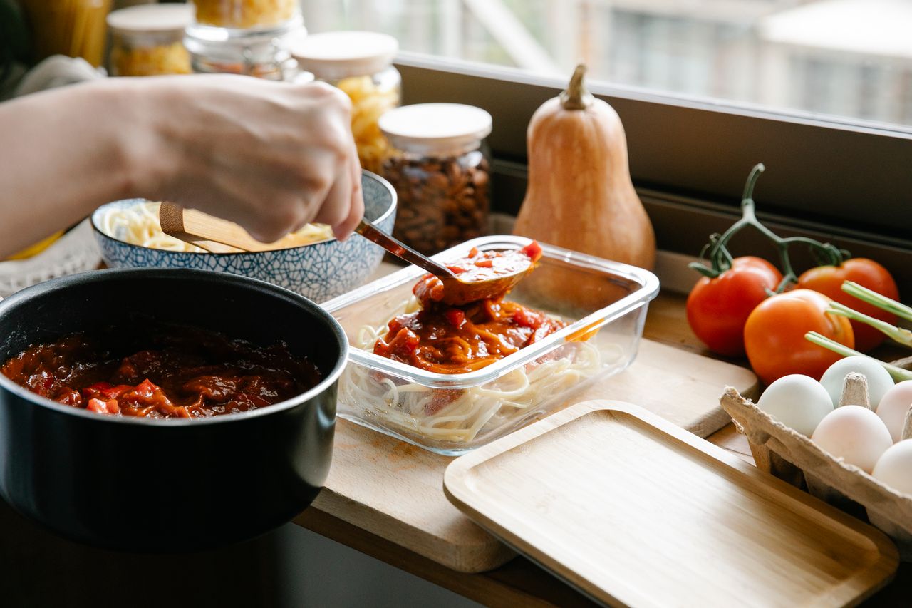 about-us-02 Unrecognizable cook pouring tasty sauce from saucepan into container with pasta while cooking at counter with ingredients in light kitchen