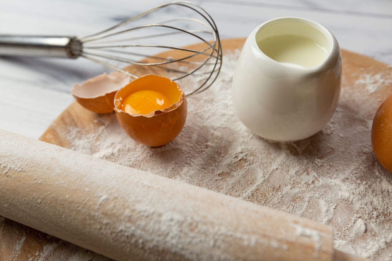 Close-up of baking ingredients including egg yolk, flour, and milk on a wooden surface.